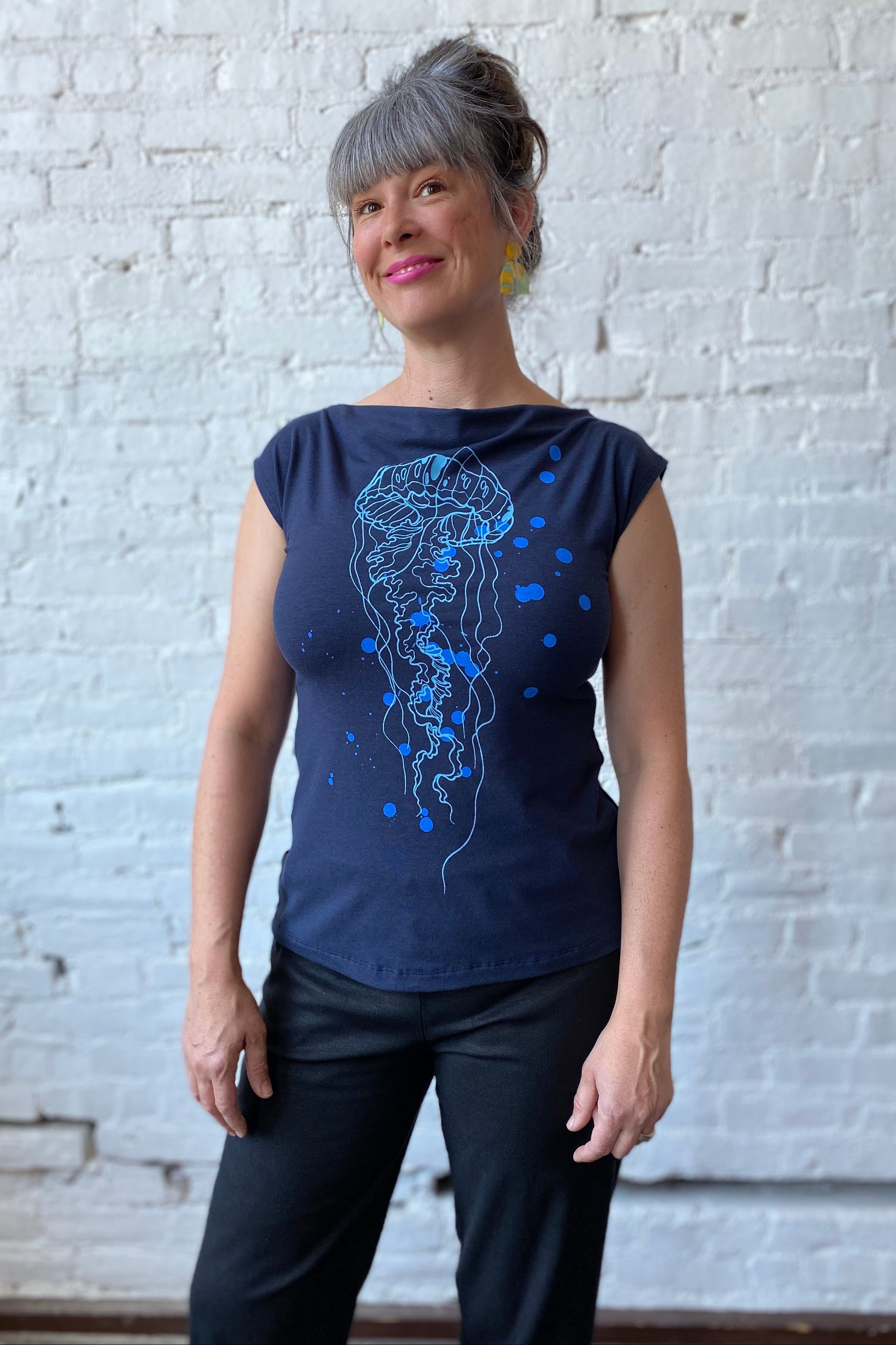 Smiling woman models sleeveless tee with large jellyfish print on front of shirt.