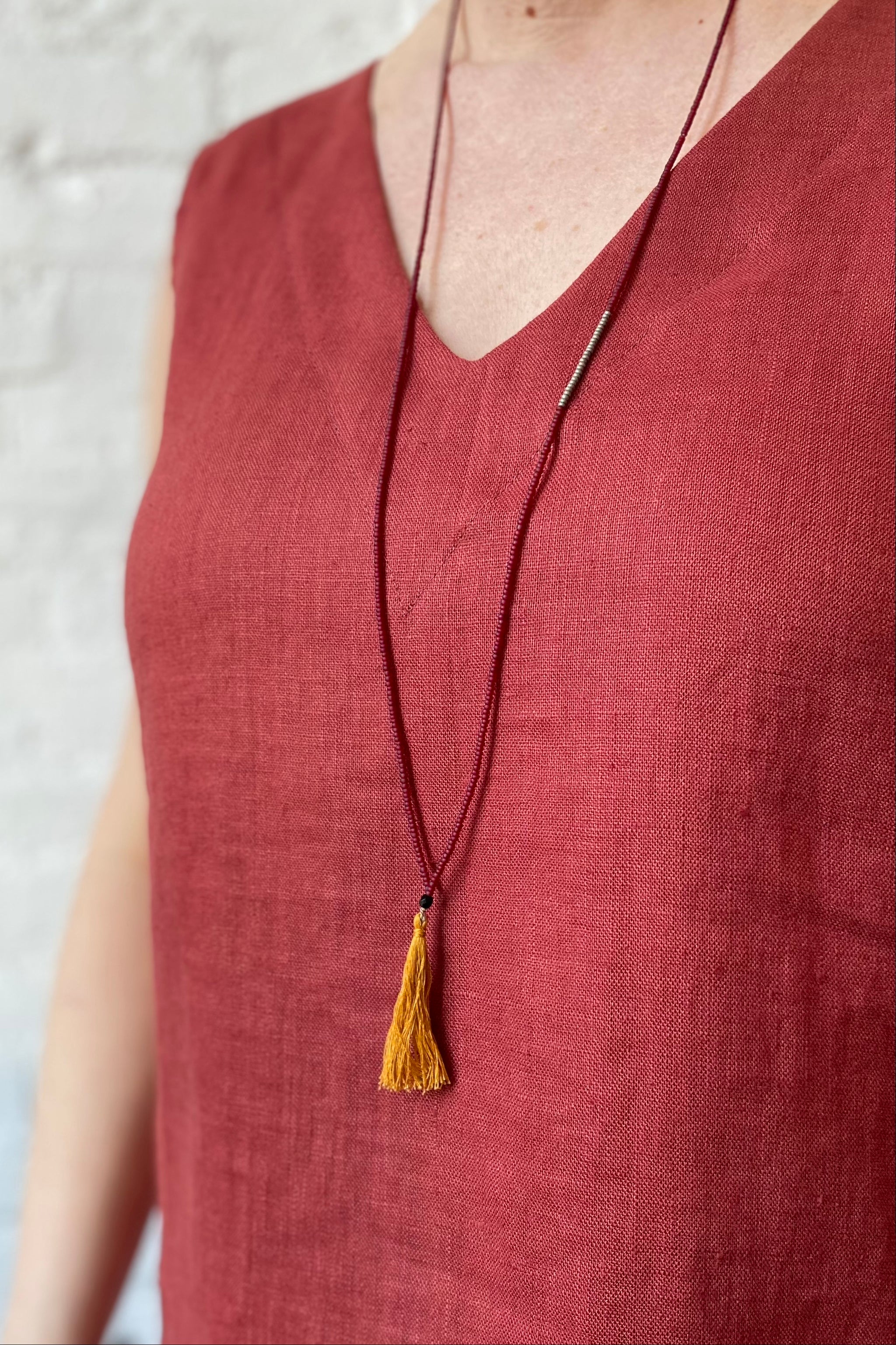 Long beaded necklae with a fringe tassel worn over a linen top.