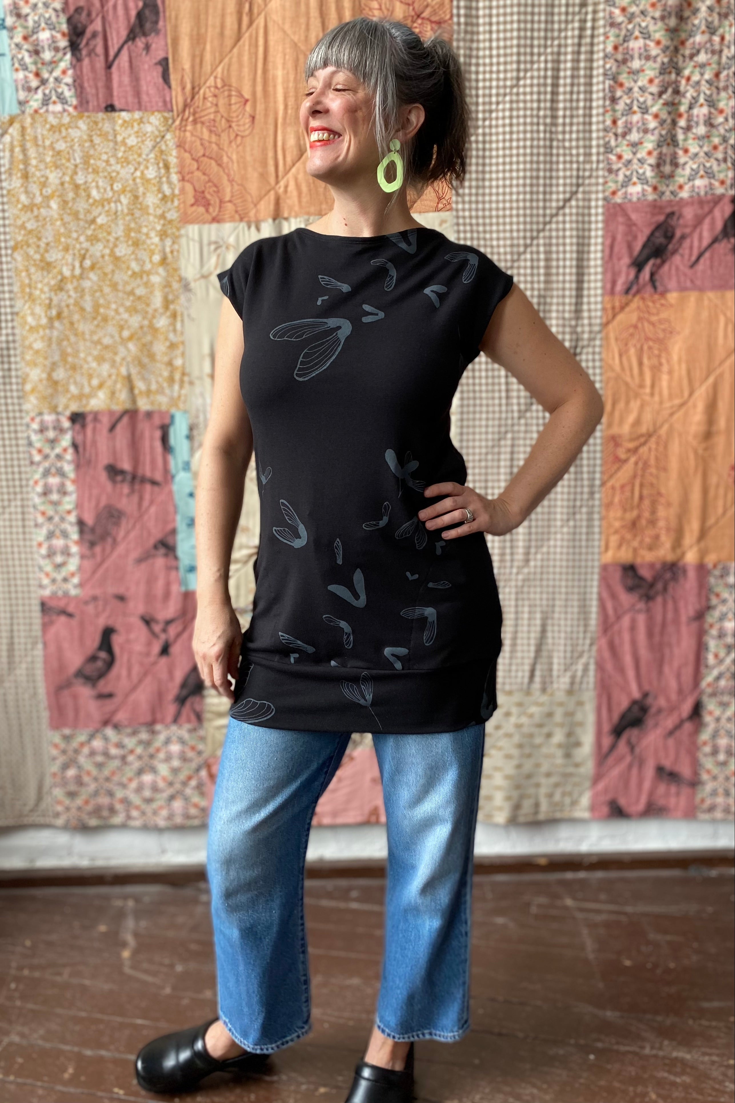 Woman models a black tunic with large grey maple pods silkscreen pattern. 